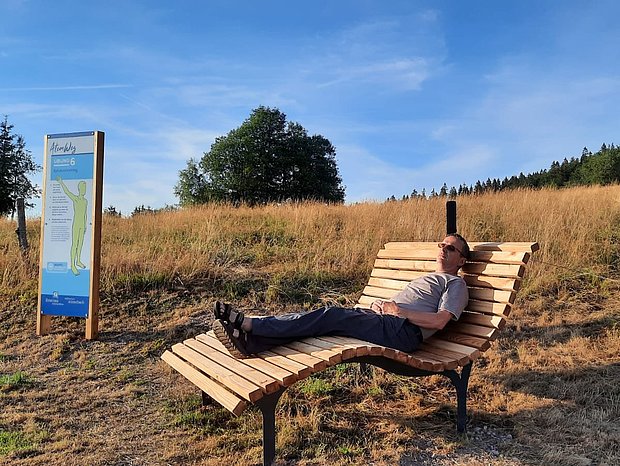 Mann sitzt auf einer Holzliege im Wald und entspannt