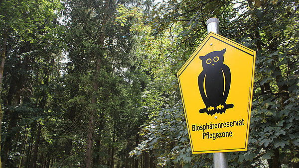 Schild mit Naturschutzeule und Text Biosphärenreservat Pflegezone an Waldrand