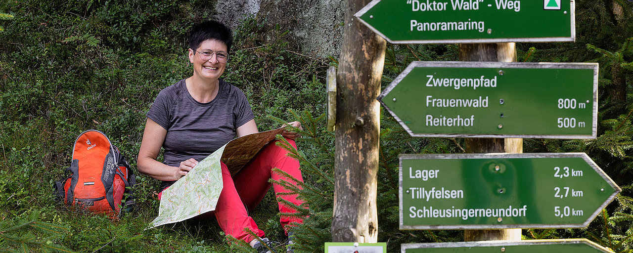 Frau studiert Karte neben Wanderwegweiser