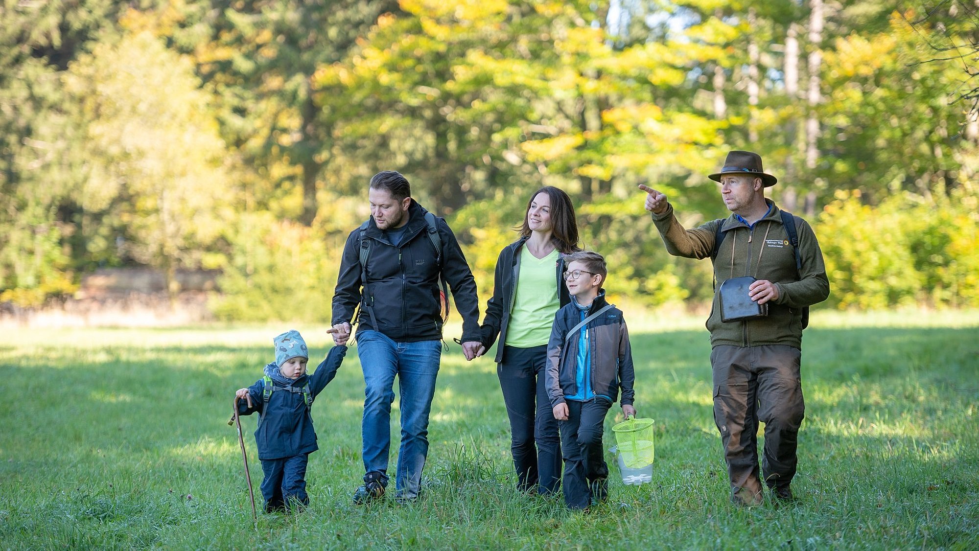 Eine Familie ist mit einem Ranger bei einer Wanderung auf einer Wiese