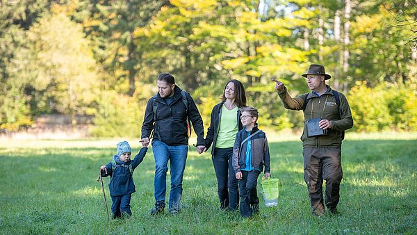 Eine Familie ist mit einem Ranger bei einer Wanderung auf einer Wiese