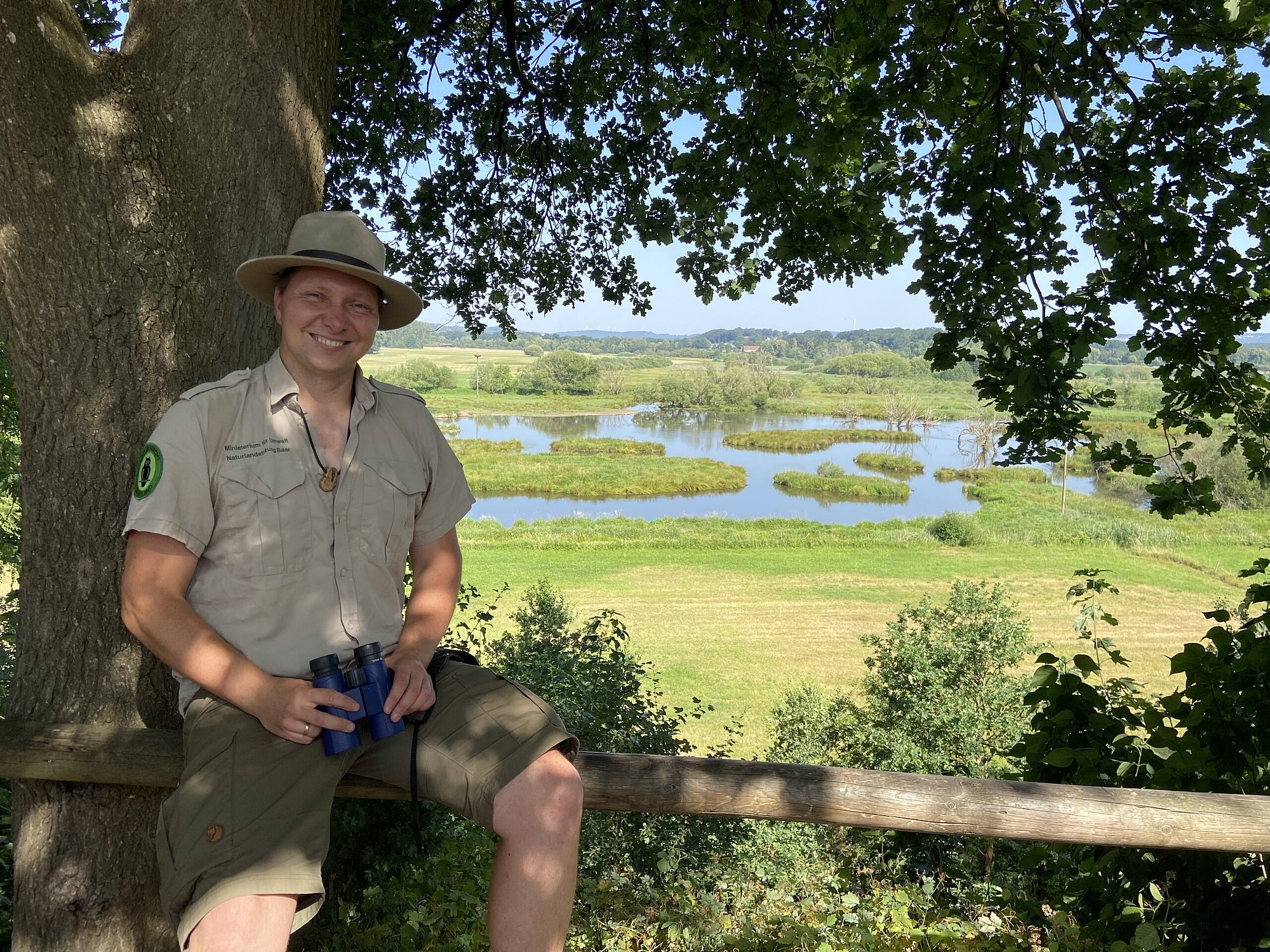 Mann sitzt unter Baum mit Blick auf Feuchwiese